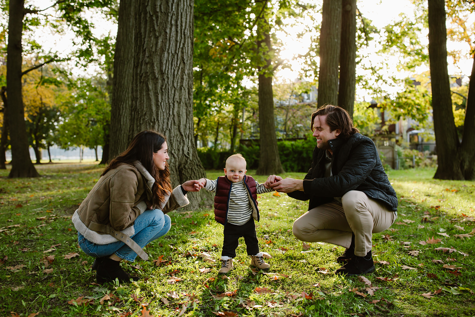 Mother and Father helping their baby son walk during a photo shoot in a park